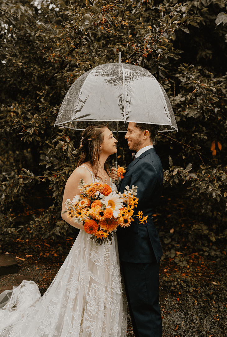 Couple Holding Clear Umbrella And Orange Bouquet On Rainy Wedding Day